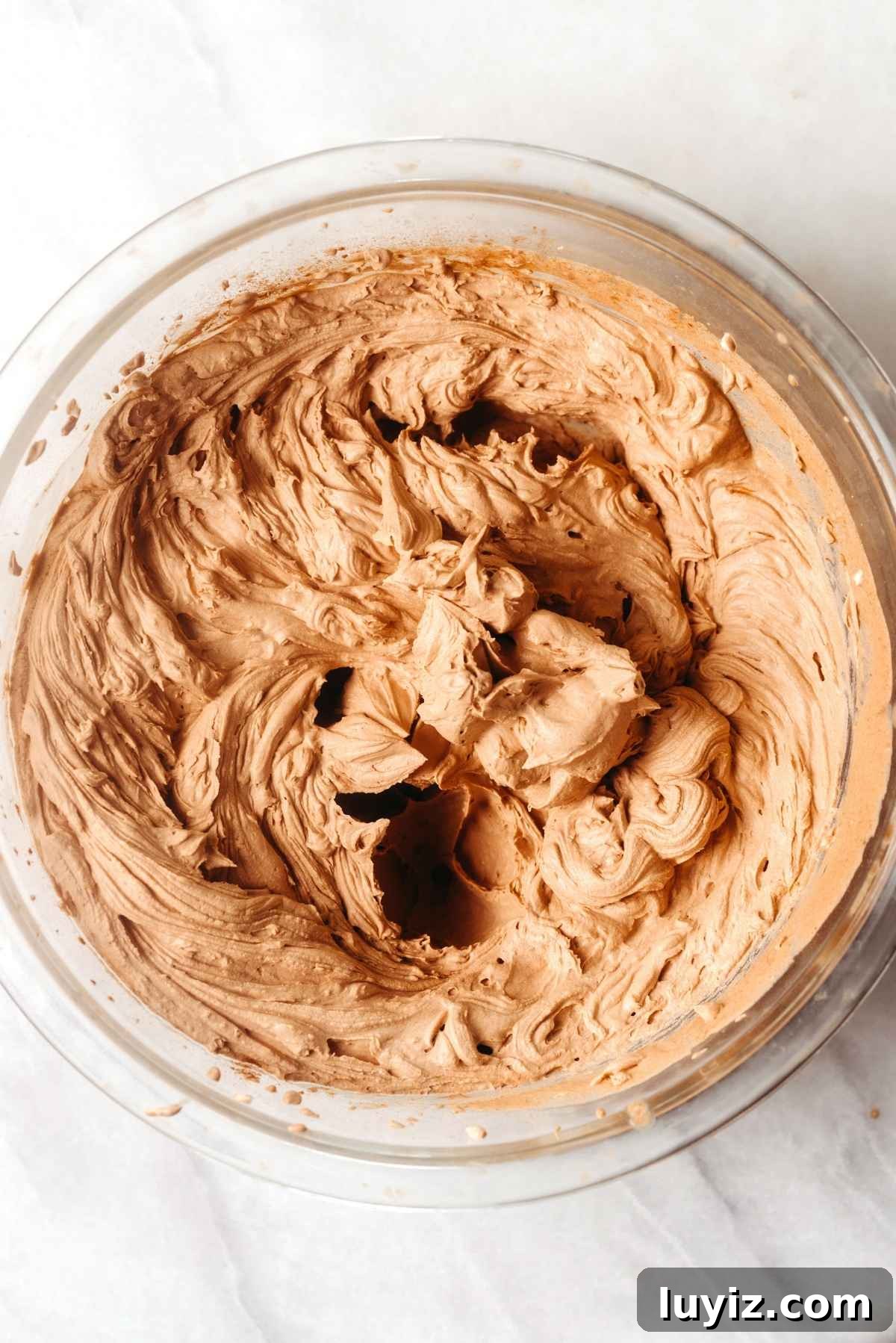 Fudgy Brownie Bites Recipe — Moist Mini Chocolate Brownies 17 Chocolate mascarpone whipped cream in a large chilled glass mixing bowl on a white textured background.