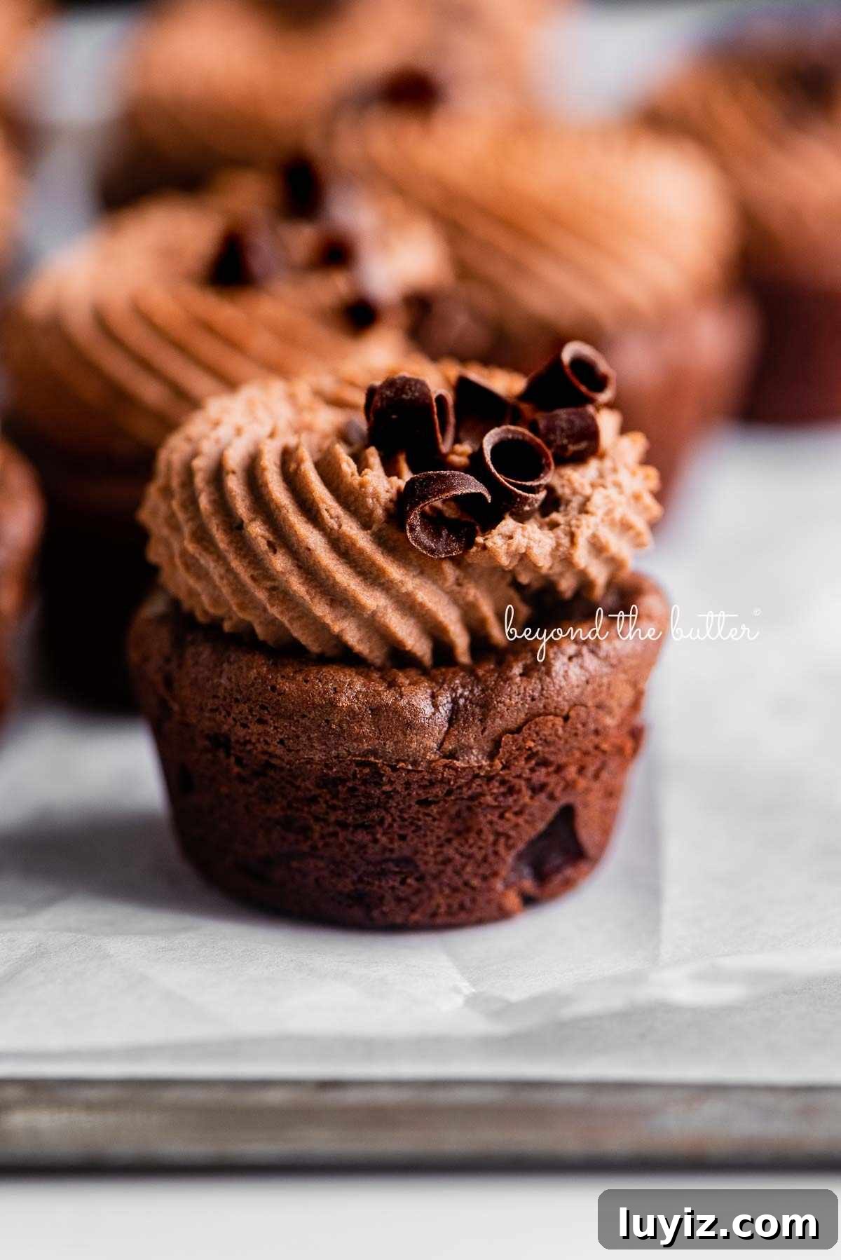 Fudgy Brownie Bites Recipe — Moist Mini Chocolate Brownies 19 Brownie bites topped with chocolate mascarpone whipped cream and chocolate curls randomly placed on crinkled white parchment paper.