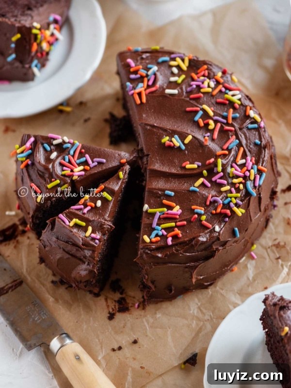 Fudgy Brownie Bites Recipe — Moist Mini Chocolate Brownies 23 Angled image of sliced single layer chocolate cake on parchment paper with slices of cake on small dessert plates around it and a knife on parchment paper.