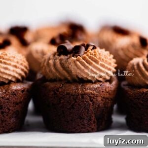 Fudgy Brownie Bites Recipe — Moist Mini Chocolate Brownies 24 Fudgy brownie bites topped with chocolate mascarpone whipped cream and chocolate curls placed together on a parchment paper lined baking sheet.