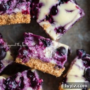 Blueberry Swirl Cheesecake Bars Recipe — Creamy Layered Dessert 14 Sliced blueberry swirl cheesecake bars randomly placed in a vintage baking tin.