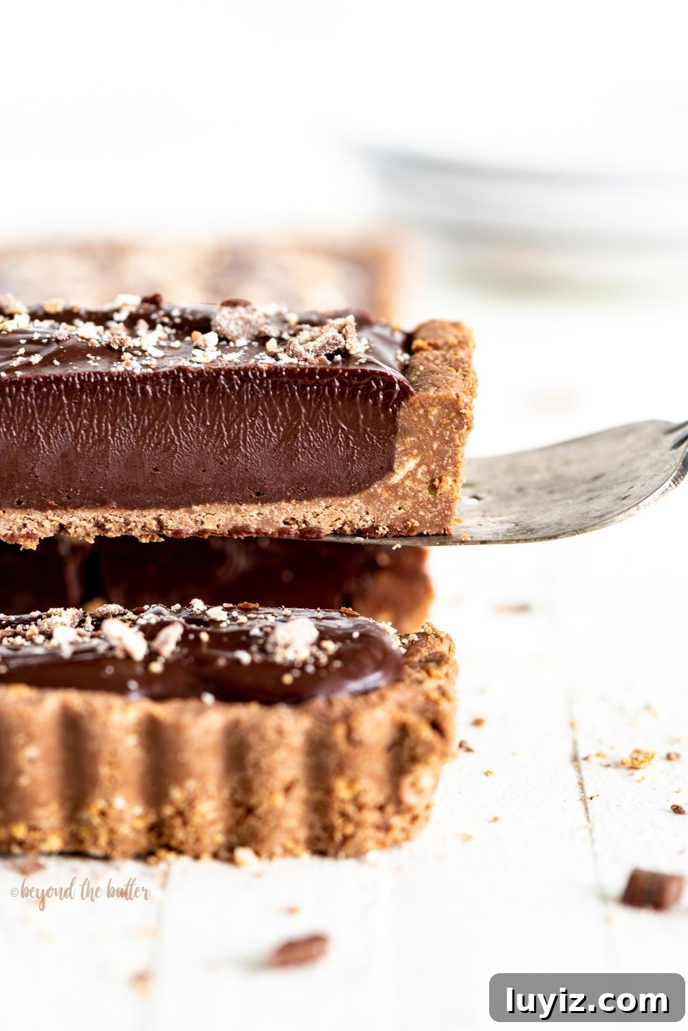 Decadent No-Bake Dark Chocolate Tart Recipe 2 No-bake Dark Chocolate Tart | Close-up photo of a slice of no-bake dark chocolate tart being lifted up with a serving utensil