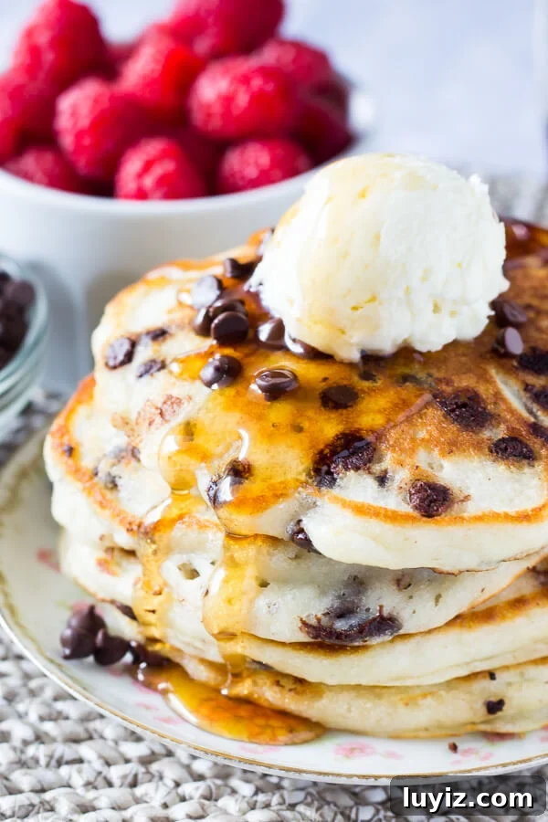 A stack of fluffy buttermilk chocolate chip pancakes drenched in syrup and topped with whipped butter.