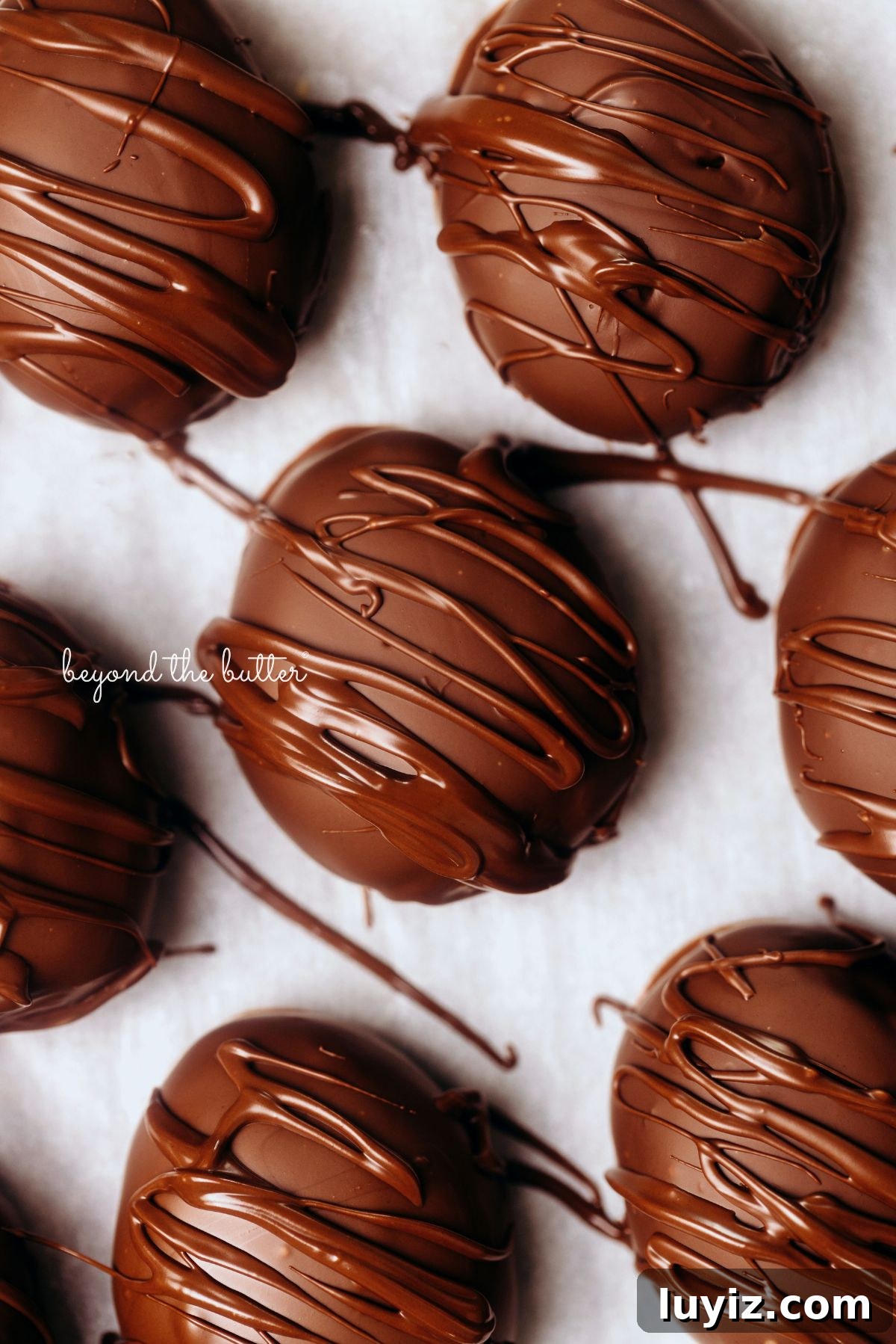 Peanut Butter Eggs Dipped in Chocolate: Homemade Candy Recipe 2 Chocolate covered peanut butter eggs drizzled in extra chocolate and placed on wax paper lined background.
