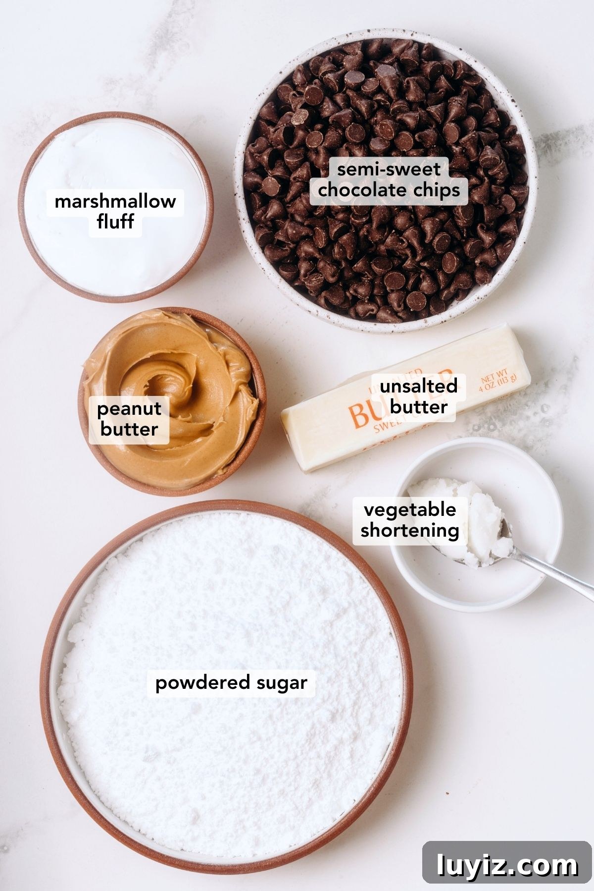 Peanut Butter Eggs Dipped in Chocolate: Homemade Candy Recipe 4 Ingredients in various size bowls labeled as semi-sweet chocolate chips, peanut butter, marshmallow fluff, unsalted butter, powdered sugar, and vegetable shortening on a white marbled background.
