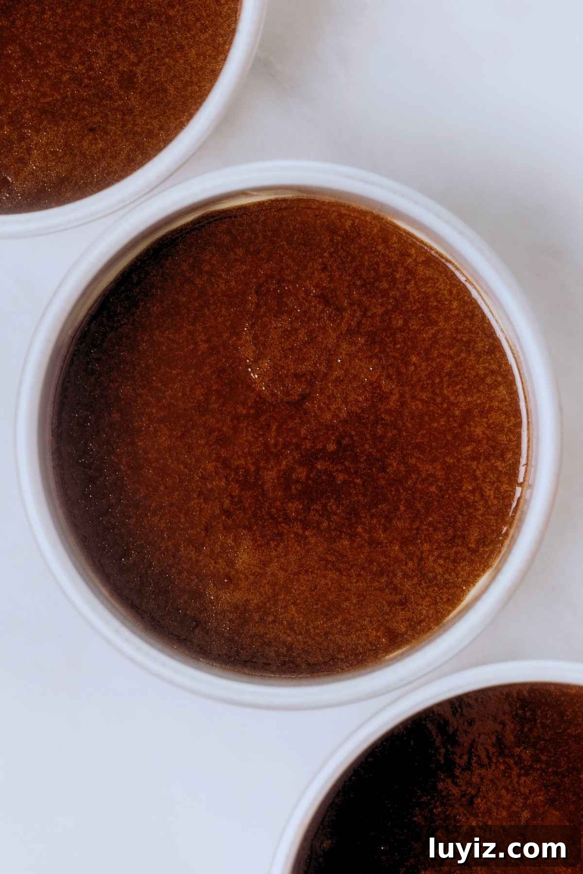 Decadent Chocolate Cake with Oreo Buttercream Frosting 12 Three metal cake tins filled with chocolate cake batter on a white background.