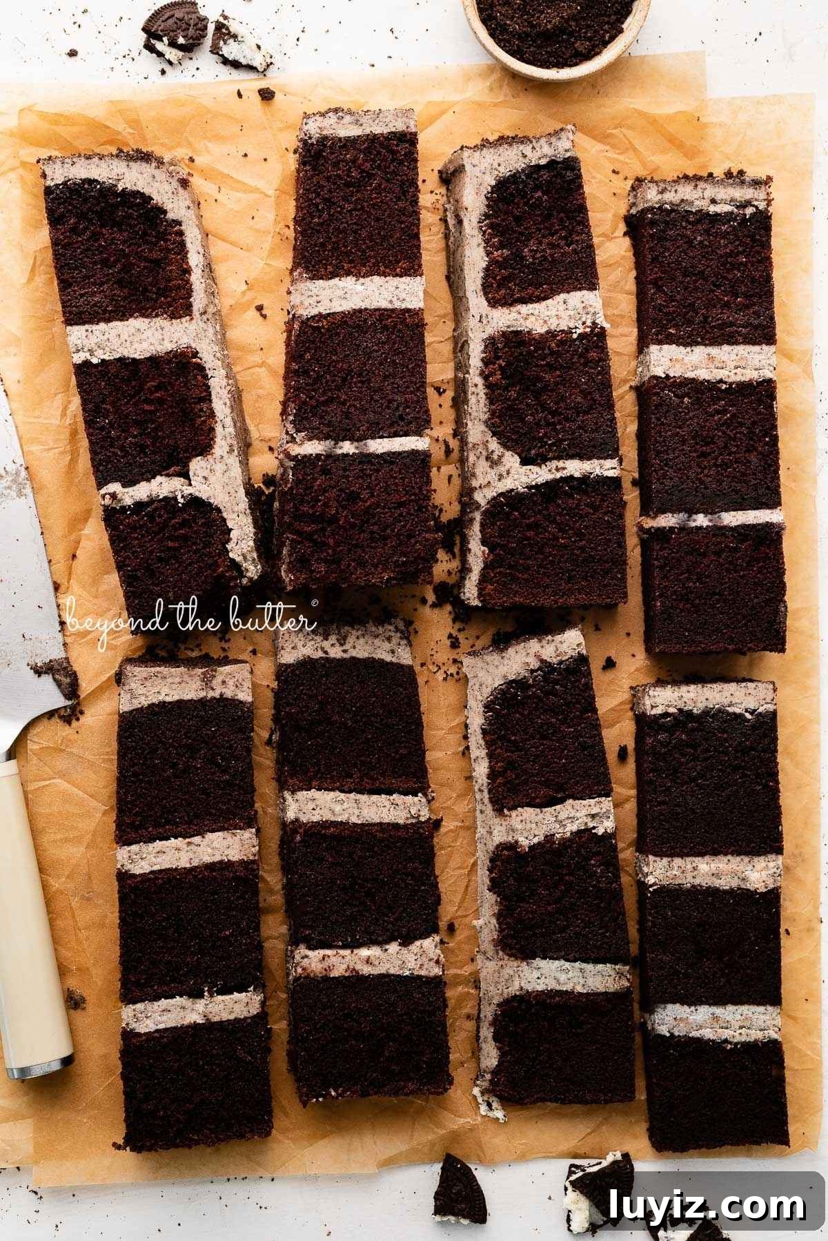 Decadent Chocolate Cake with Oreo Buttercream Frosting 19 Slices of chocolate oreo cake on natural parchment paper with bits of oreo crumbs and a knife placed next to the cake.