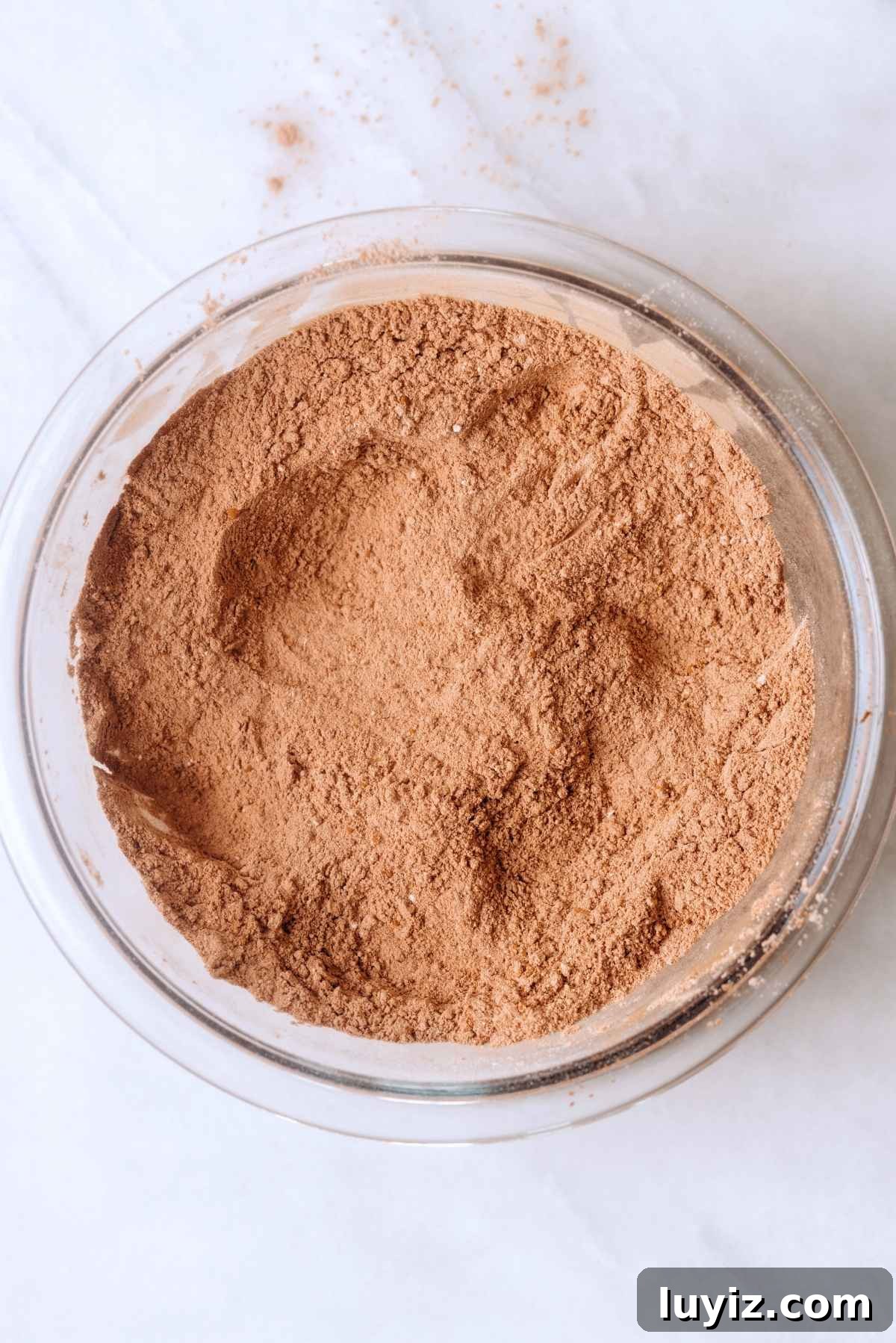 Decadent Chocolate Cake with Oreo Buttercream Frosting 6 Whisked all purpose flour, baking soda, baking powder, and unsweetened cocoa powder in a large glass mixing bowl on a white and beige marbled background.