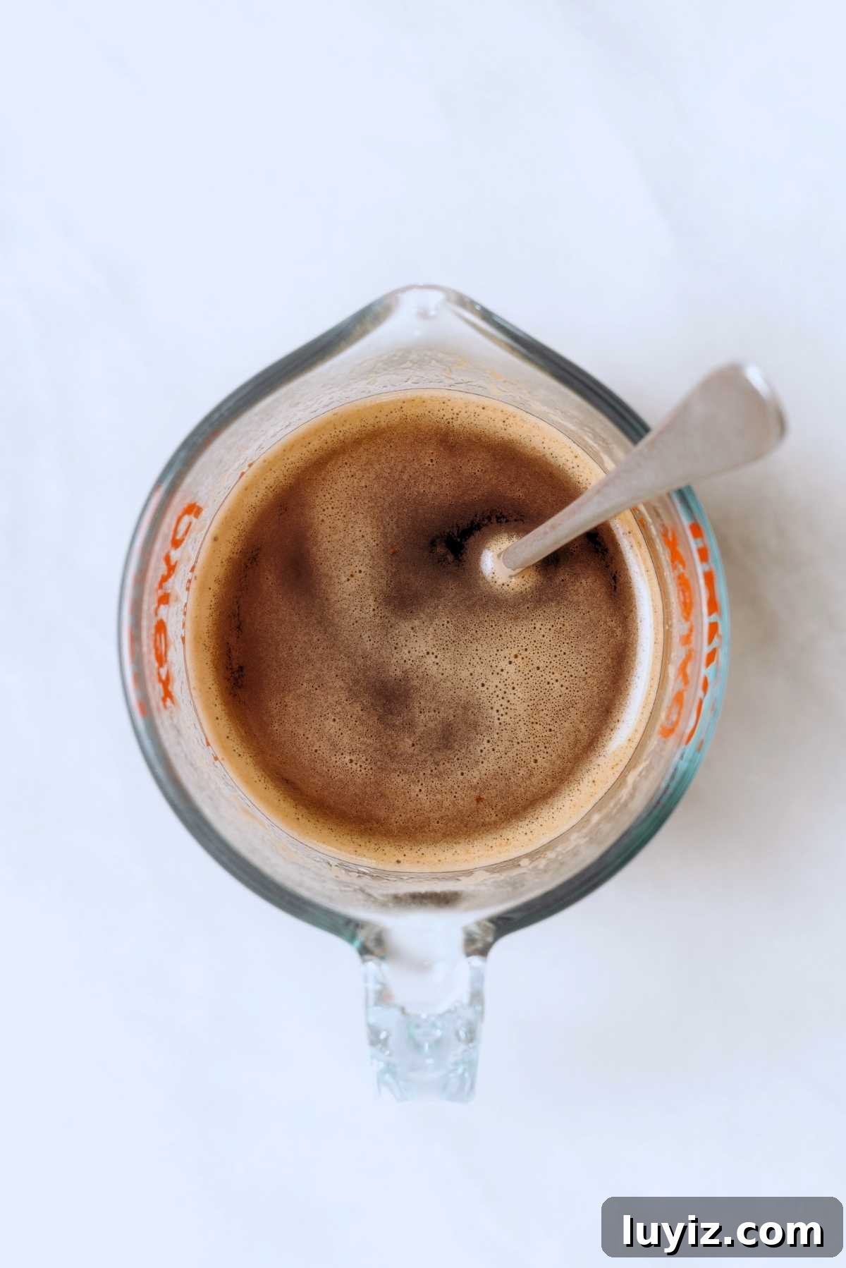 Decadent Chocolate Cake with Oreo Buttercream Frosting 8 Espresso powder and boiling water stirred together in a glass measuring cup with a spoon on a white background.