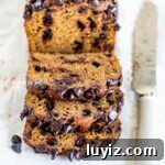 Sliced chocolate chip pumpkin bread with knife and sprinkled chocolate chips on parchment paper lined table.