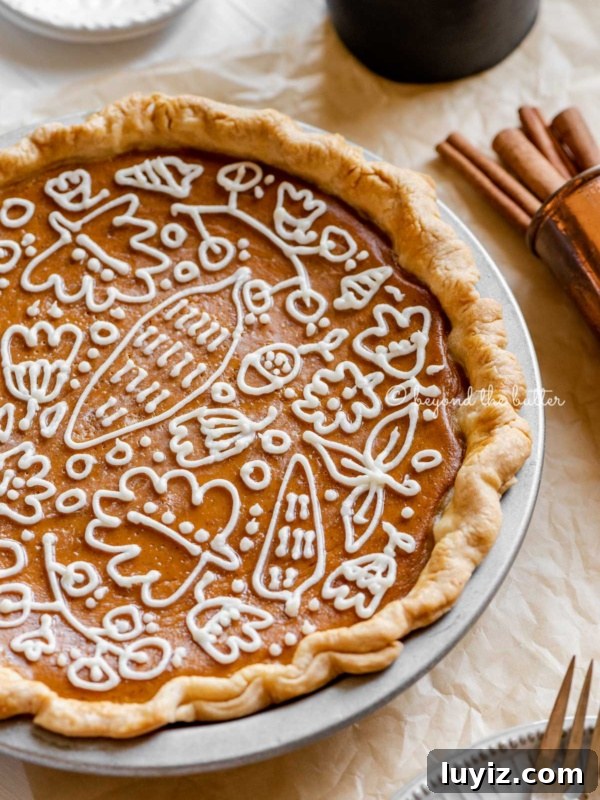 Classic Homemade Apple Pie Recipe for Perfect Crust and Filling 11 Angled image of pumpkin pie with a piped cream cheese frosting decoration surrounded by forks, cinnamon sticks, plates, and small pitcher of milk.