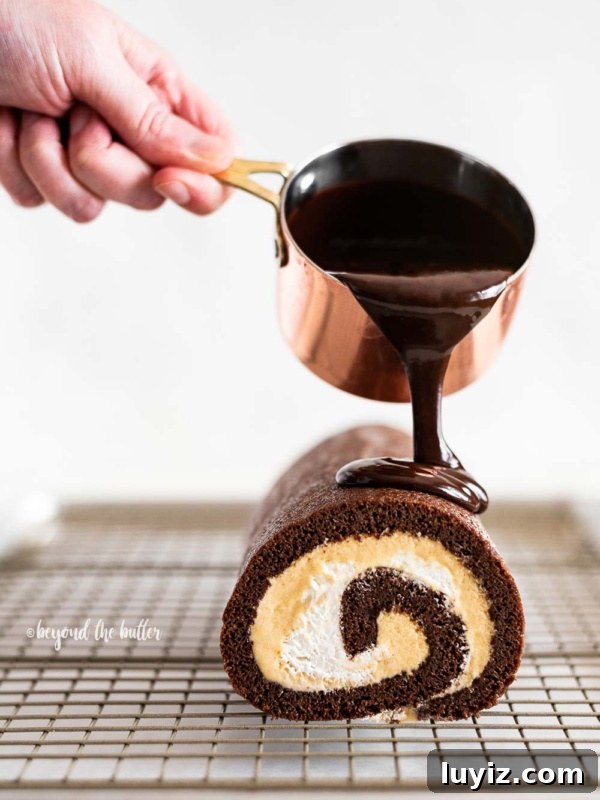 Apple Cider Whoopie Pies with Cinnamon Buttercream Filling 11 Pouring melted chocolate from small copper pot over chocolate pumpkin roll on wire cooling rack.