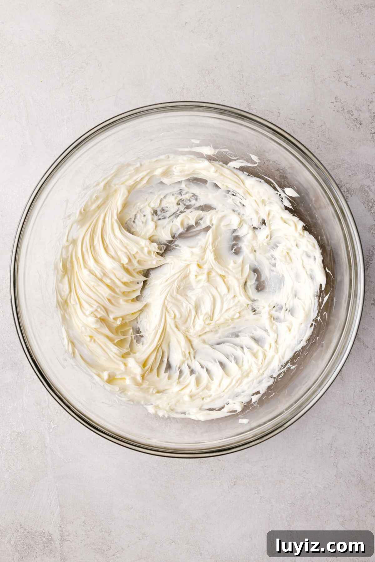Butterscotch Krimpet Sheet Cake Recipe — Moist Retro Dessert 13 Unsalted butter whisked until fluffy in a large glass mixing bowl on a white and grey textured background.