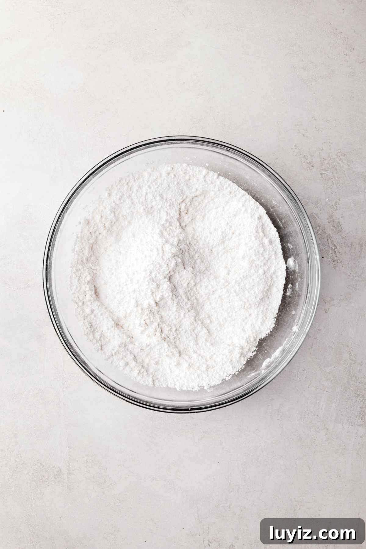 Butterscotch Krimpet Sheet Cake Recipe — Moist Retro Dessert 6 Whisked cake flour, baking powder, and salt in a small glass mixing bowl on a white and grey textured background.