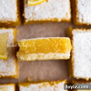 Simple Homemade Lemon Bars – Zesty Citrus Dessert Recipe 15 Sliced super easy lemon bars on parchment paper with the center lemon bar on its side.