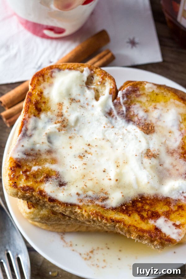 Eggnog French Toast Recipe: Festive Holiday Brunch Idea 4 Overhead shot of a plate of eggnog French toast with whipped cream melting into the bread and maple syrup.
