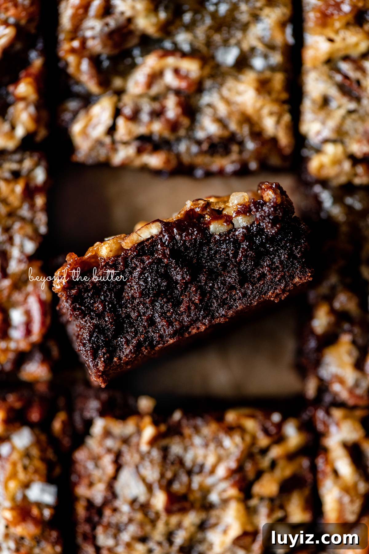 Salted Pecan Pie Brownies Recipe: Gooey Chocolate with Crunch 9 Salted pecan pie brownies placed on brown parchment paper with the center brownie placed on its side | © Beyond the Butter®