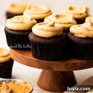 Decadent Chocolate Cupcakes with Peanut Butter Frosting 11 Wood cake stand with devil's food cupcakes surrounded by other cupcakes, peanut butter, and a napkin on a white background.