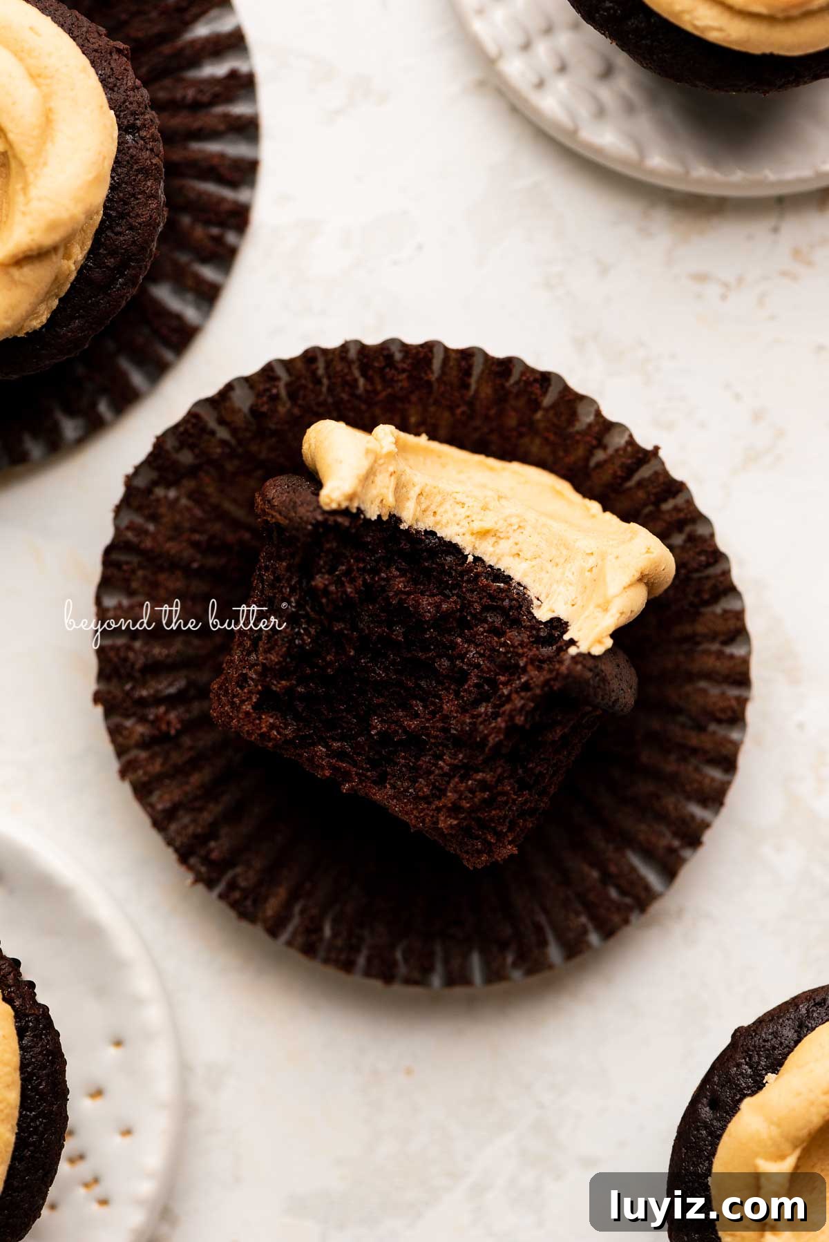 Decadent Chocolate Cupcakes with Peanut Butter Frosting 4 Unwrapped devil's food cupcake with peanut butter frosting with a bite taken out of it on white background | © Beyond the Butter®