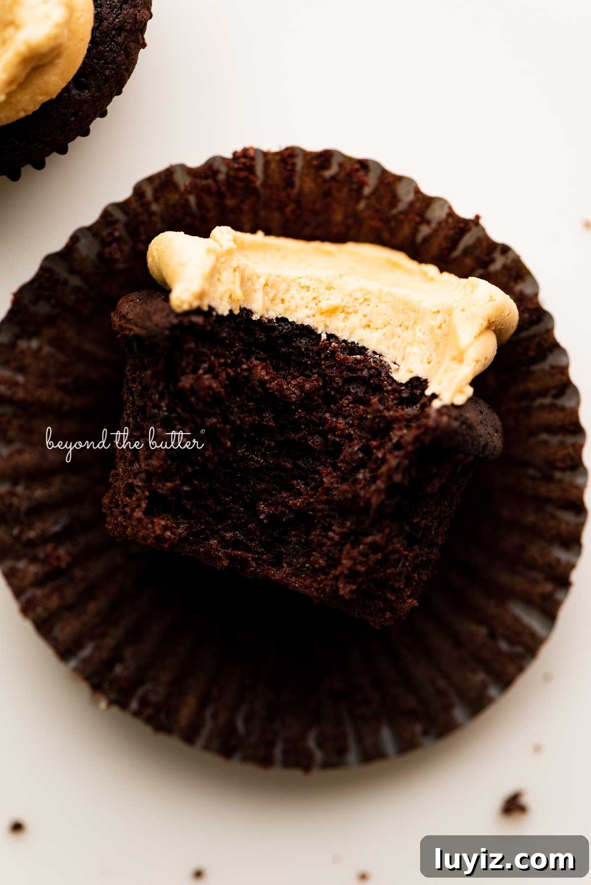 Decadent Chocolate Cupcakes with Peanut Butter Frosting 6 Unwrapped devil's food cupcake with peanut butter frosting with a bite taken out of it on white background | © Beyond the Butter®