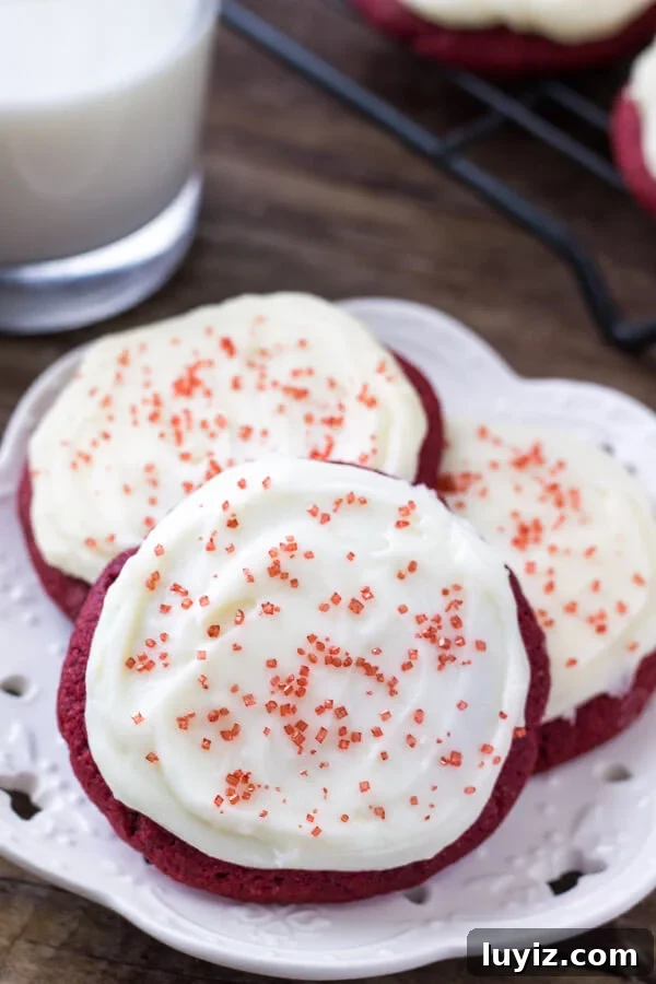Red Velvet Cookies with Cream Cheese Frosting Recipe 3 A plate of red velvet cookies with cream cheese frosting. Glass of milk and cooling rack of cookies in the background.