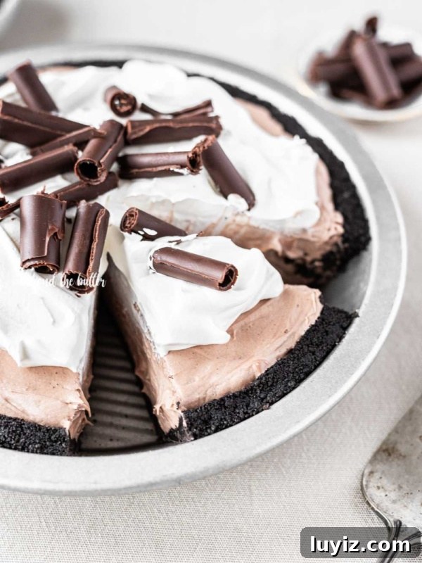 Angled image of sliced no-bake chocolate cream pie with chocolate wafer crust and garnished with Cool Whip and chocolate curls.