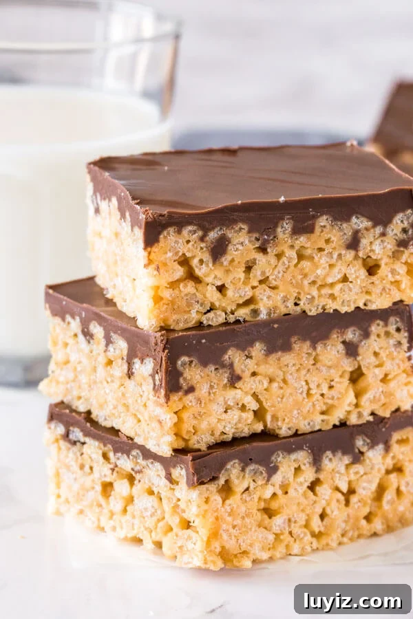 Peanut Butter Rice Krispie Treat Recipe — Chewy No-Bake Bars 2 A stack of 3 peanut butter rice krispie treats with a layer of chocolate on top of each.