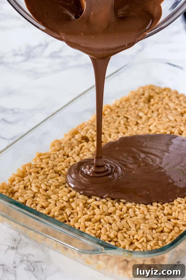 Peanut Butter Rice Krispie Treat Recipe — Chewy No-Bake Bars 3 Pouring the chocolate topping over a pan of peanut butter rice krispie treats.