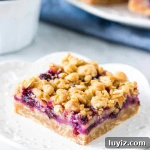 Slice of blueberry oatmeal crumble bar on a plate with bowl of berries.
