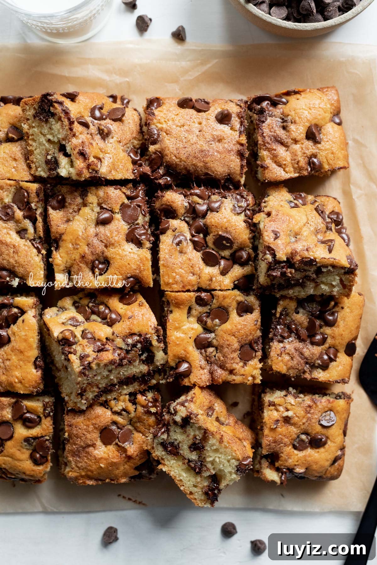 Moist Chocolate Chip Sour Cream Coffee Cake Recipe 4 Cut squares of chocolate chip sour cream coffee cake on brown parchment paper with bowl of chocolate chips | © Beyond the Butter®