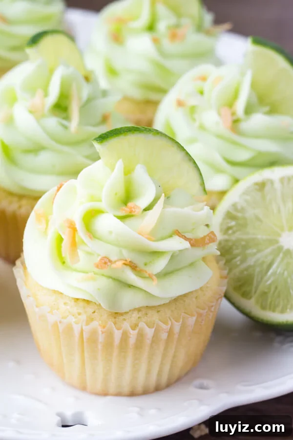 Coconut Cupcakes with Zesty Lime Buttercream Frosting 3 A white plate of coconut cupcakes with lime frosting and a lime.