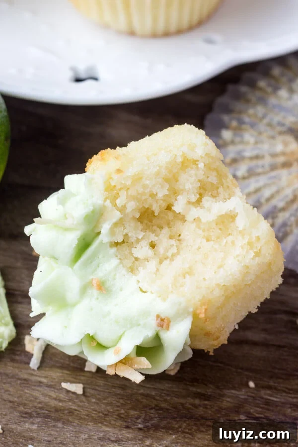 Coconut Cupcakes with Zesty Lime Buttercream Frosting 6 Coconut Cupcakes with Lime Frosting won it's side with muffin paper removed and bite taken out of it. Plate of cupcakes in the background