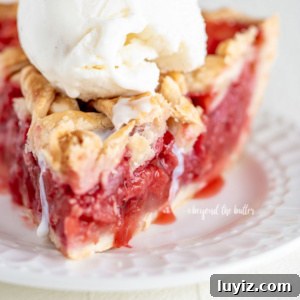 Classic Strawberry Rhubarb Pie Recipe for Perfect Spring Baking 12 Slice of strawberry rhubarb pie with scoop of vanilla ice cream on dessert plate on white wood table.