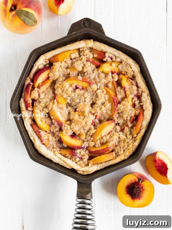 Classic Strawberry Rhubarb Pie Recipe for Perfect Spring Baking 9 Brown sugar peach crumble pie in cast iron pan with sliced peaches on white wood table.