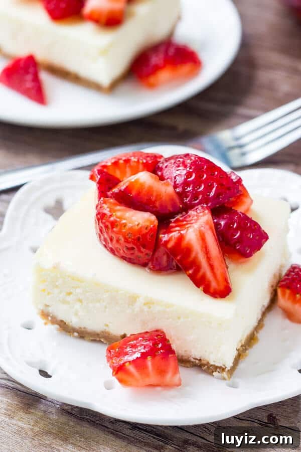 Strawberry Cheesecake Bars with Graham Cracker Crust 2 Cheesecake bar topped with chopped strawberries on a white plate. Fork and second cheesecake bar in the background.