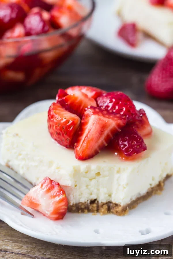 Strawberry Cheesecake Bars with Graham Cracker Crust 3 Slice of strawberry cheesecake bar with bite taken out of it and a bowl of chopped strawberries.