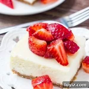 Strawberry Cheesecake Bars with Graham Cracker Crust 6 Cheesecake bar topped with chopped strawberries on a white plate. Fork and second cheesecake bar in the background.