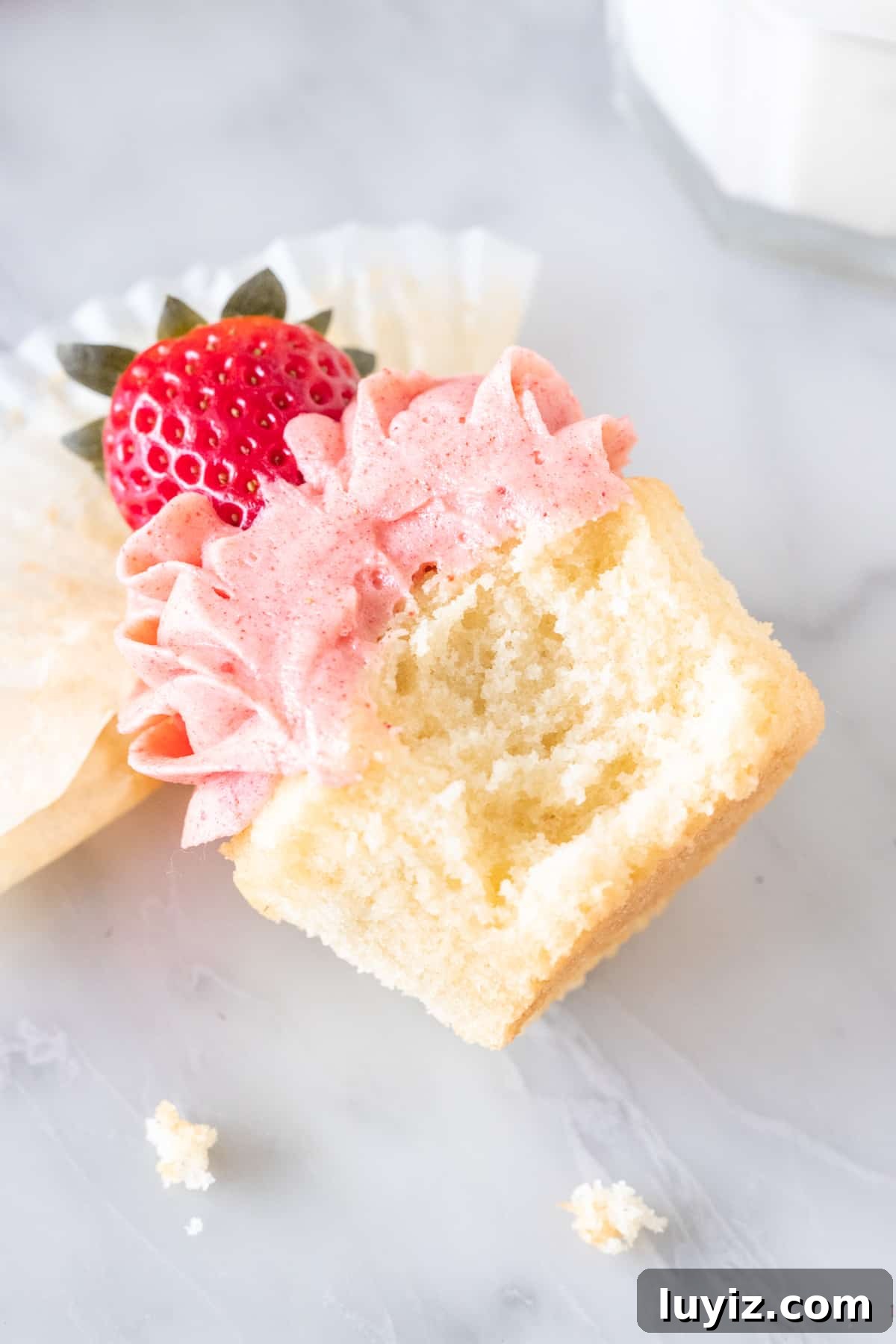Vanilla Cupcakes with Fresh Strawberry Buttercream Frosting 6 Cupcake on its side with a bite taken out.