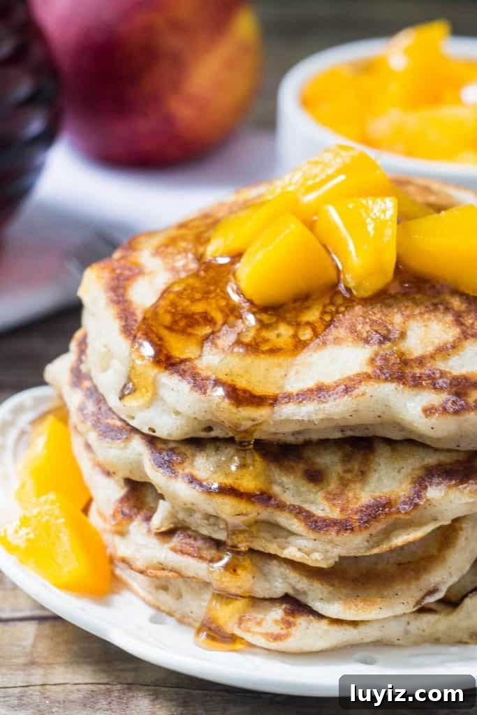 Brown Sugar Peach Pancakes Recipe with Caramelized Peaches 2 Stack of brown sugar peach pancakes drizzled with syrup and topped with chopped peaches. Jar of syrup of bowl of chopped peaches in the background.