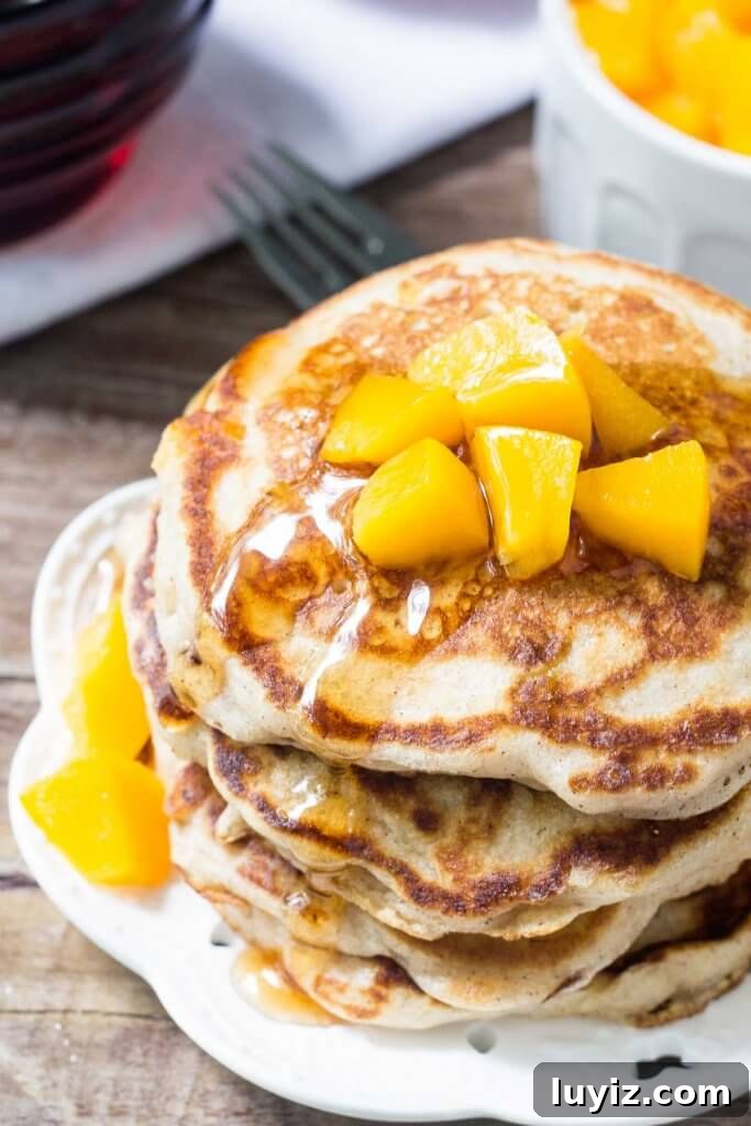 Brown Sugar Peach Pancakes Recipe with Caramelized Peaches 3 Overhead view of a stack of brown sugar peach pancakes on a white plate & drizzled with syrup and chopped peaches.