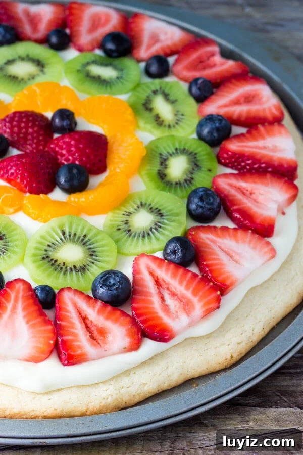 Sugar Cookie Fruit Pizza Recipe — Fresh Fruit Dessert Pizza Guide 2 Whole sugar cookie fruit pizza topped with strawberries, blueberries, kiwis and mandarin oranges in its pizza pan.