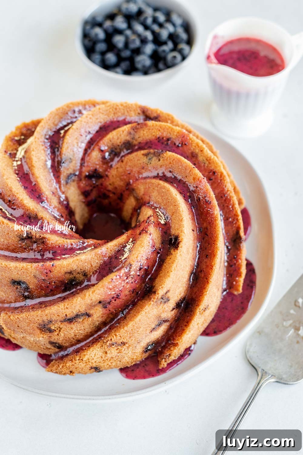 Moist Blueberry Bundt Cake with Lemon Glaze 2 Angled image of super easy blueberry bundt cake with blueberry glaze drizzled over the top | All Images © Beyond the Butter, LLC