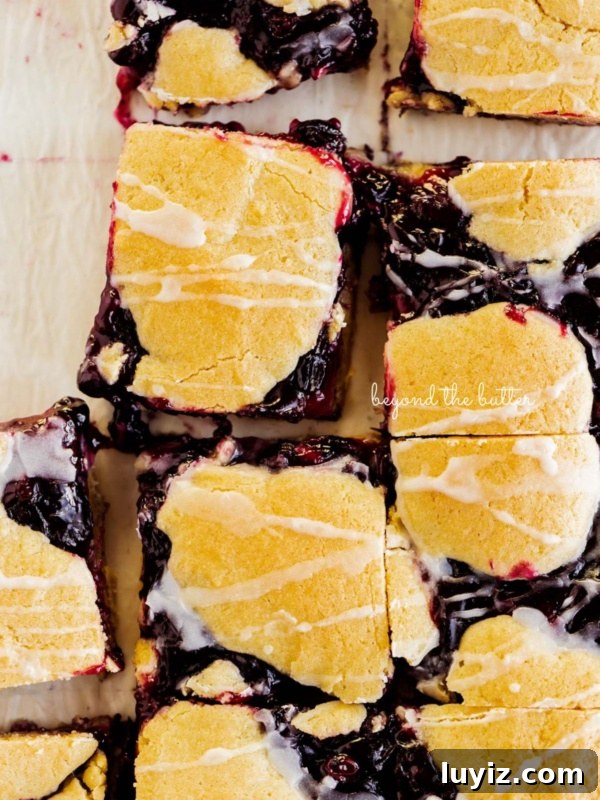 Moist Blueberry Bundt Cake with Lemon Glaze 12 Sliced blueberry swirl coffee cake squares on a white parchment paper background.