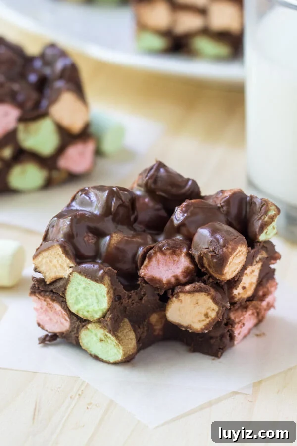 Chocolate Confetti Squares Recipe for Party Dessert Bars 5 Soft, chewy chocolate confetti square with a bite taken out of it. Second confetti square and glass of milk in the background.
