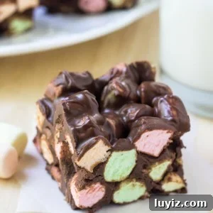 One peanut butter chocolate confetti square on a piece of wax paper. Glass of milk and plate of squares in the background.