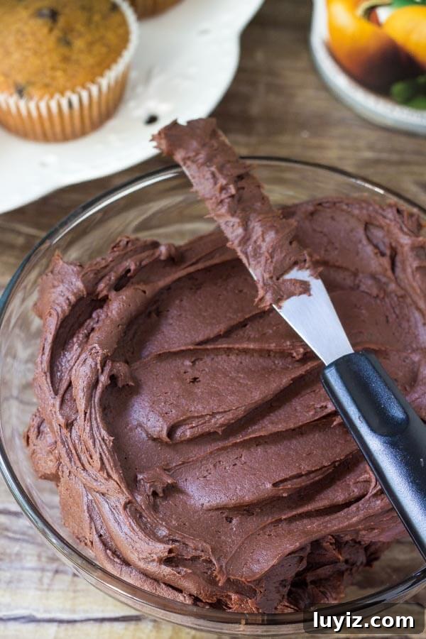 Pumpkin Chocolate Chip Cupcakes Recipe for Moist Fall Treats 5 Bowl of chocolate frosting with a plate of pumpkin chocolate chip cupcakes in the background.