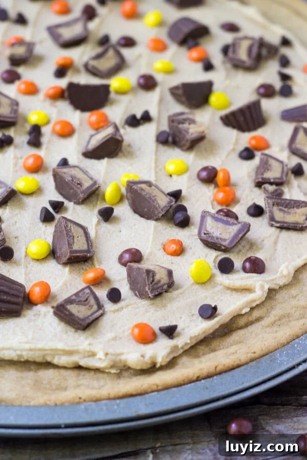 Peanut Butter Cookie Pizza Recipe: How to Make a Decadent Dessert Pizza 3 Overhead shot of full peanut butter cookie pizza on it's pizza pan. With peanut butter frosting & peanut butter candies