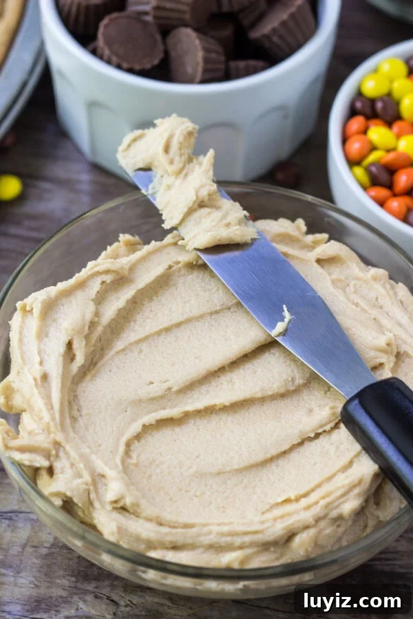Peanut Butter Cookie Pizza Recipe: How to Make a Decadent Dessert Pizza 4 Bowl of creamy peanut butter frosting with bowls of Reese's Pieces and peanut butter cups in the background.
