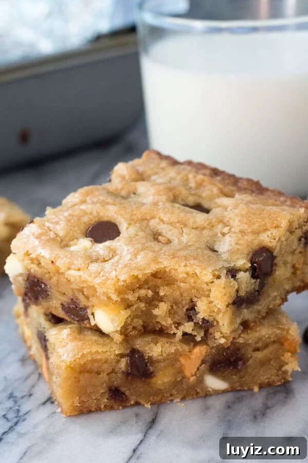 Triple-Chip Cookie Bar Recipe: Chewy Chocolate, Peanut & Butterscotch 2 Stack of 2 triple chip cookie bars with a bite taken out of the bar on top. A glass of milk and the pan in the background.