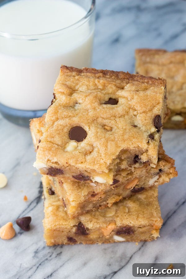 Triple-Chip Cookie Bar Recipe: Chewy Chocolate, Peanut & Butterscotch 4 Overhead shot of 3 triple chip cookie bars stacked. Glass of milk in the background.